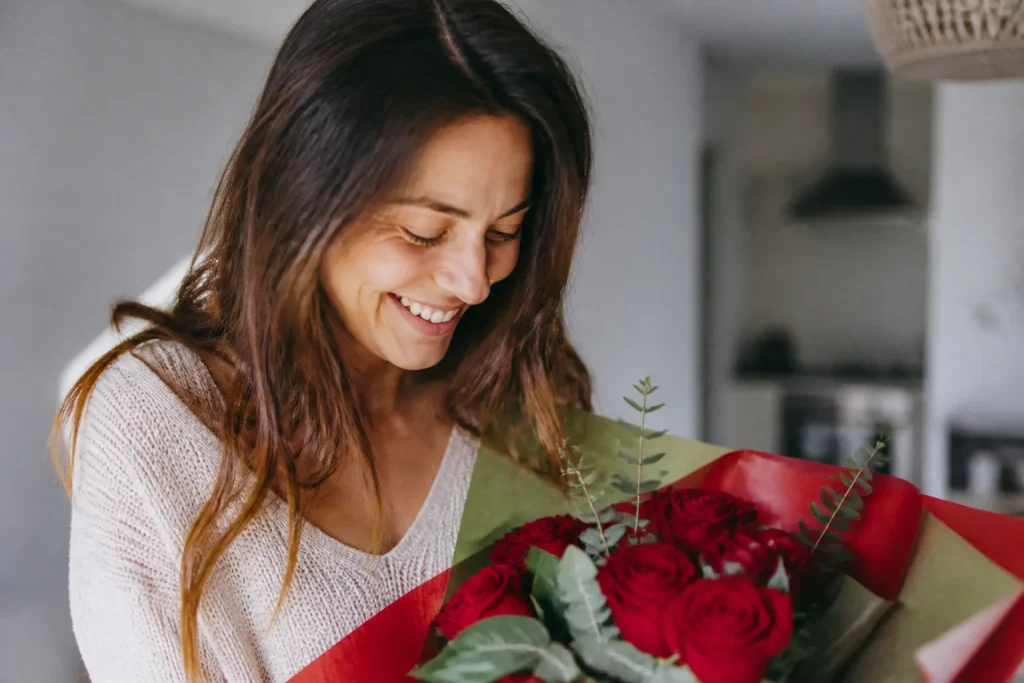 Femme qui rit devant un bouquet de fleurs rouges