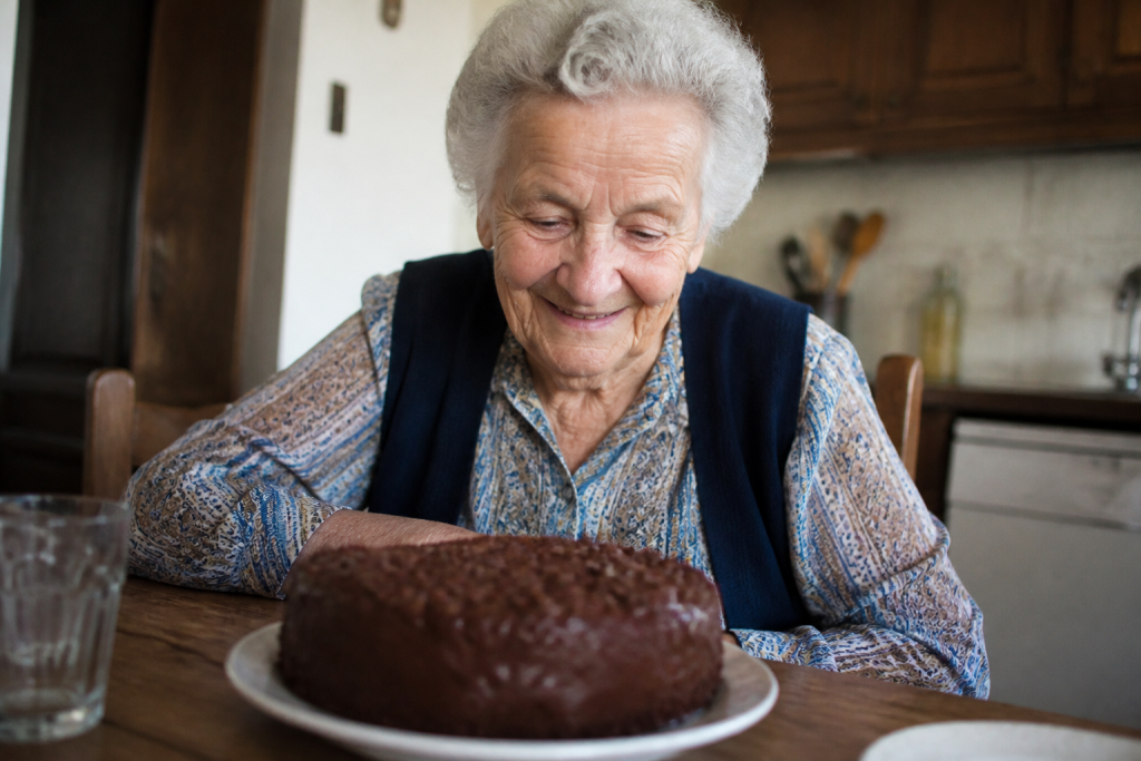 Une vieille dame sourit devant un gateau au chocolat